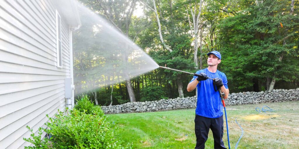 Power washing expert power washes side of grey home to clear off dirt and grime.